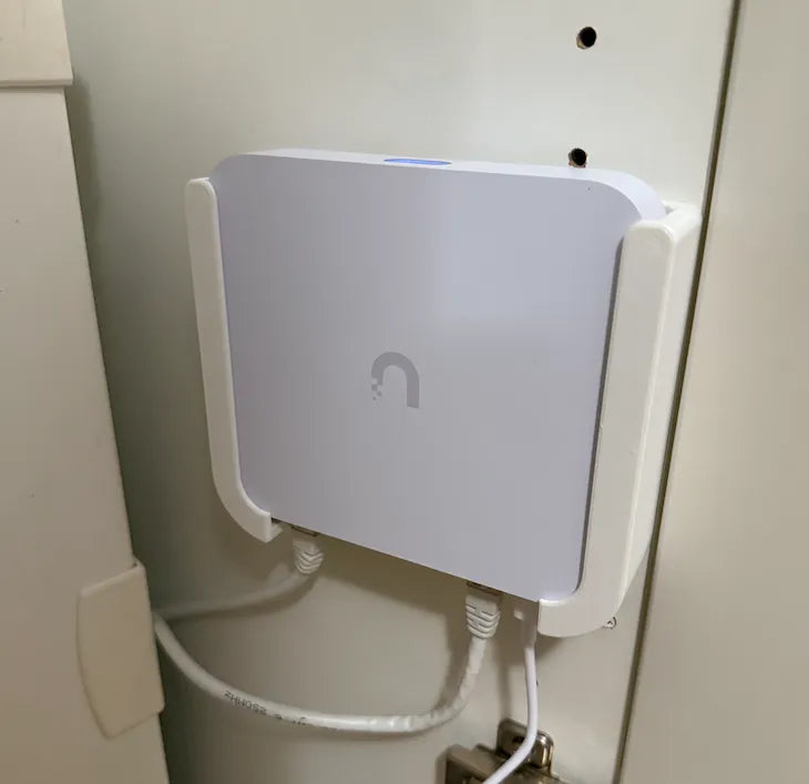 A white wall mount for Unifi Cloud Gateway Ultra device, mounted on a wall.